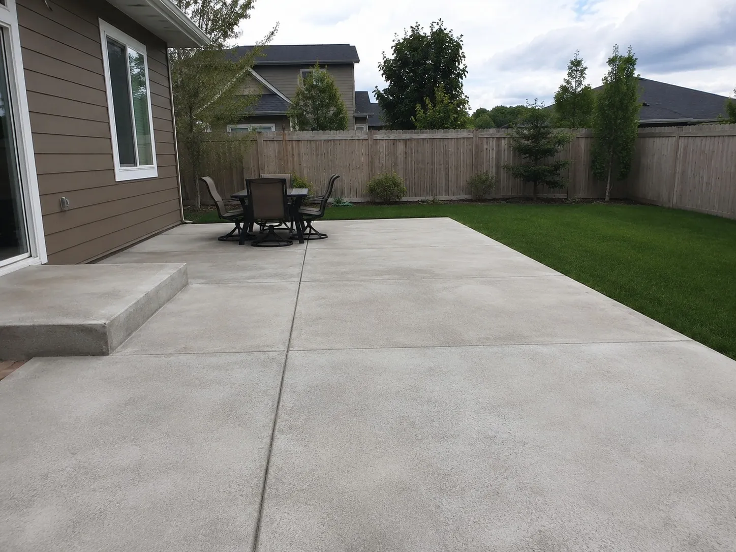 Large poured concrete patio with a dining set alongside a fenced back garden