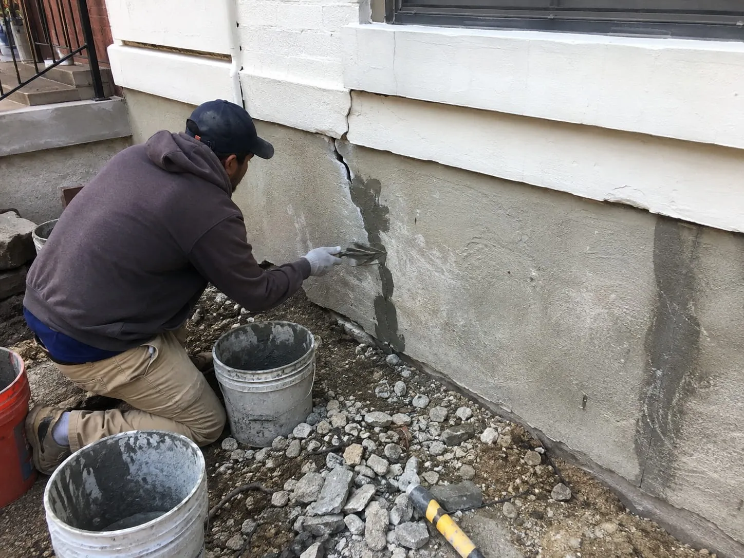 Contractor patching a crack in the parged foundation wall of a Washington DC rowhouse