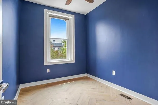 Second bedroom painted deep blue with herringbone flooring and a tall sash window