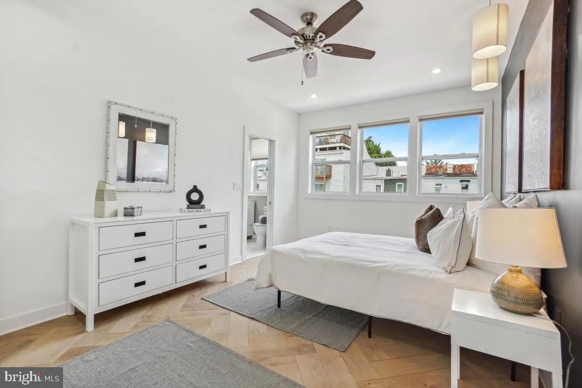 Primary bedroom with herringbone wood flooring, corner windows and an ensuite bath beyond